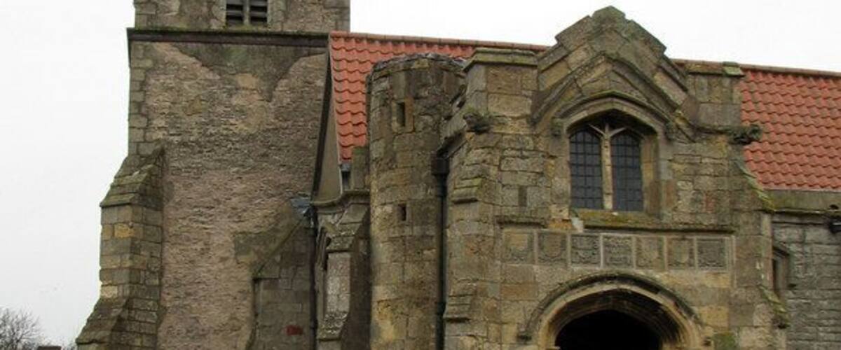 Eine historische Steinkirche mit einem hohen Glockenturm und einem roten Ziegeldach.