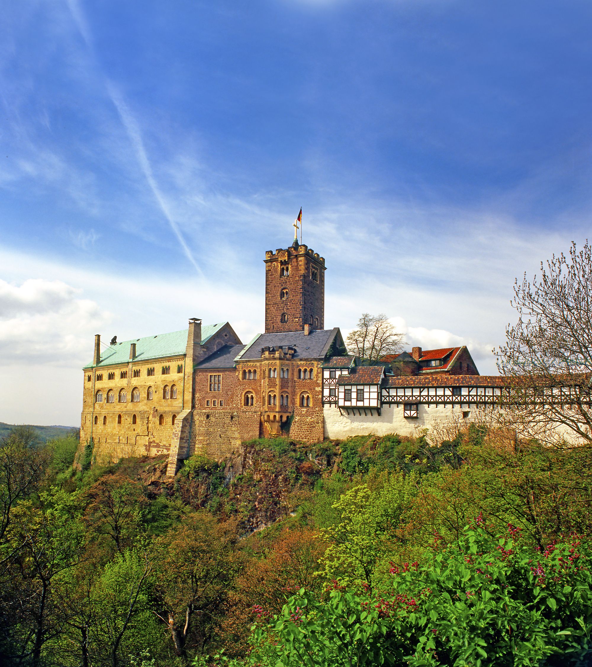 A historic castle with a prominent tower, surrounded by lush greenery and a clear sky.