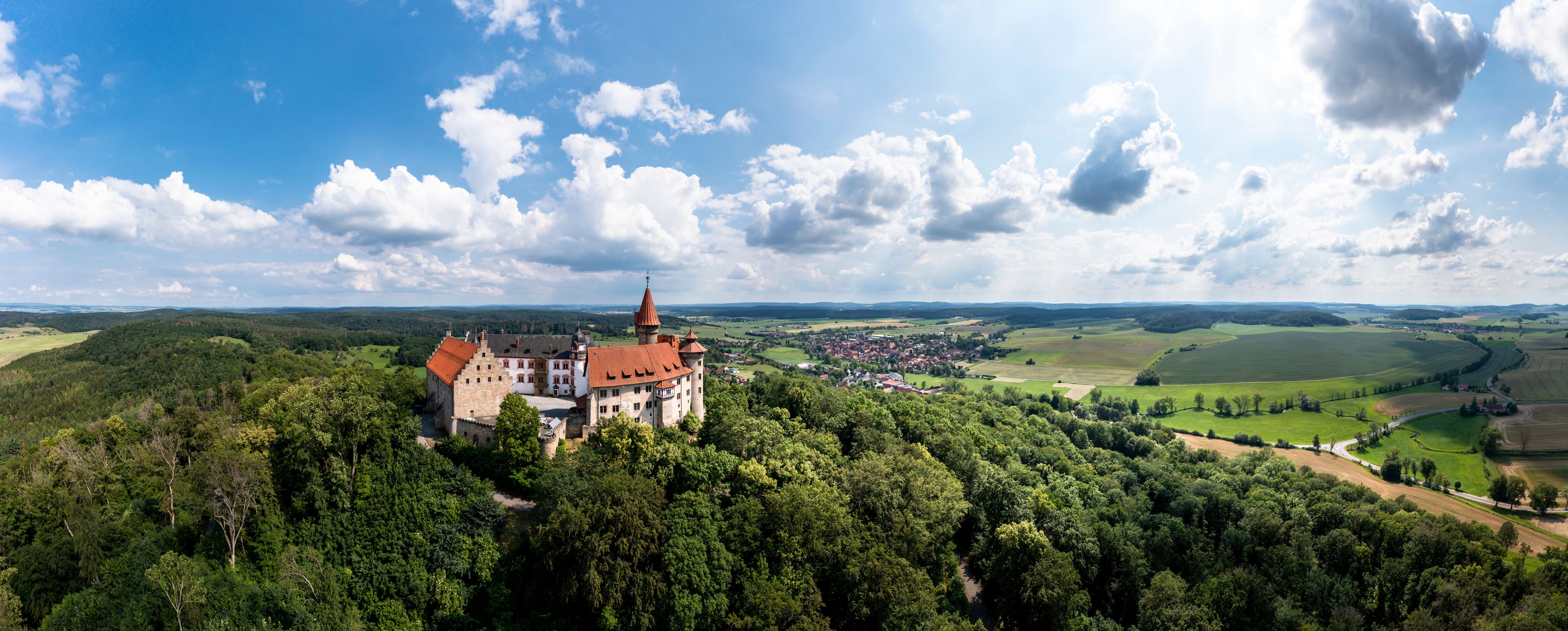 Eine Burg, umgeben von üppiger Vegetation, mit einem Dorf im Tal darunter.