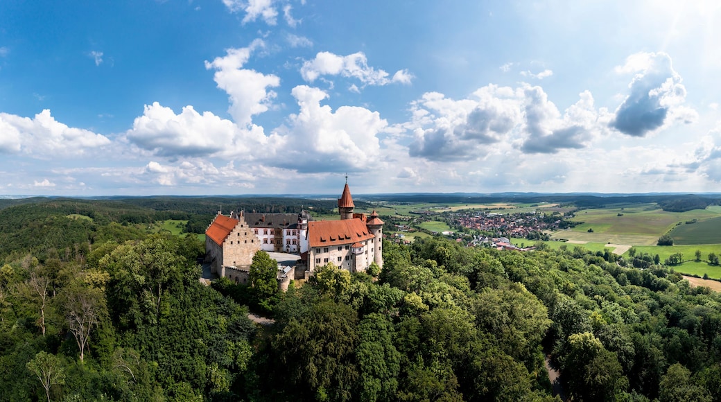 Eine Burg, umgeben von üppiger Vegetation, mit einem Dorf im Tal darunter.