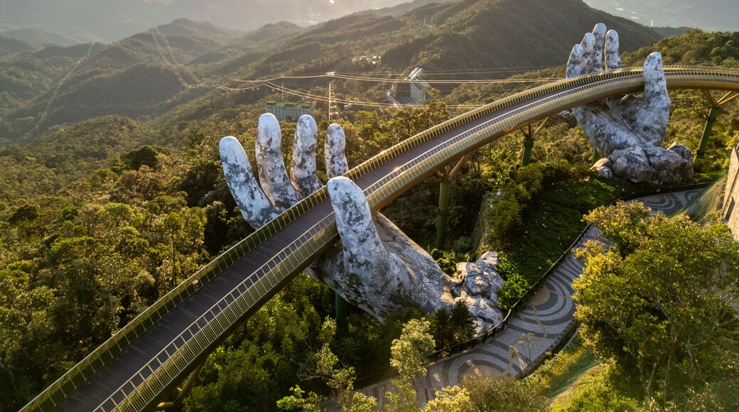 Aerial view of the iconic Golden Bridge, held by giant stone hands, stretching across the lush, sun-kissed mountains, DaNang, Da Nang, Vietnam.