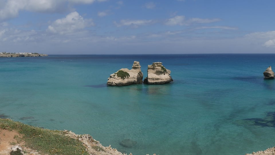 A coastal landscape with clear turquoise waters and rocky formations.