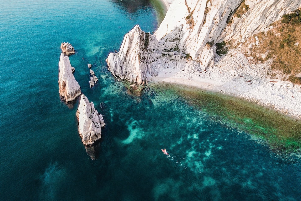 A coastal landscape with clear turquoise waters, rocky formations, and a sandy beach.
