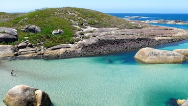 Un paisaje costero con aguas turquesas cristalinas, grandes rocas y una colina cubierta de hierba.