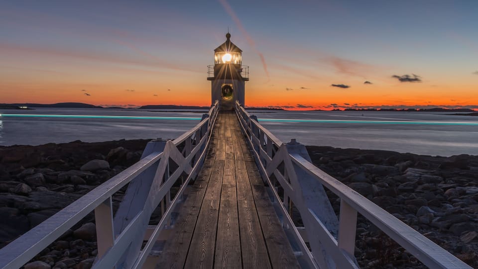 A wooden pier leading to a lighthouse at sunset.