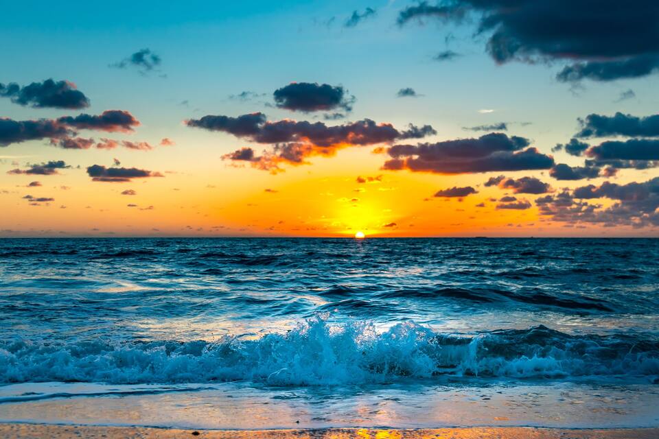 Una puesta de sol sobre el océano con olas rompiendo en la orilla.