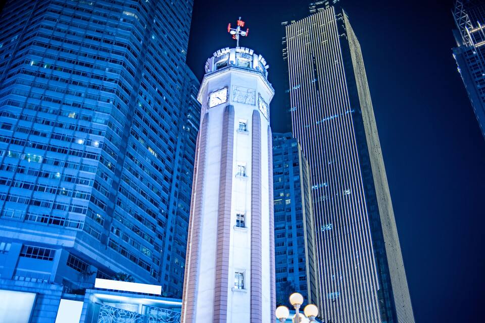Una vista nocturna de un paisaje urbano con una imponente torre de reloj y rascacielos modernos.