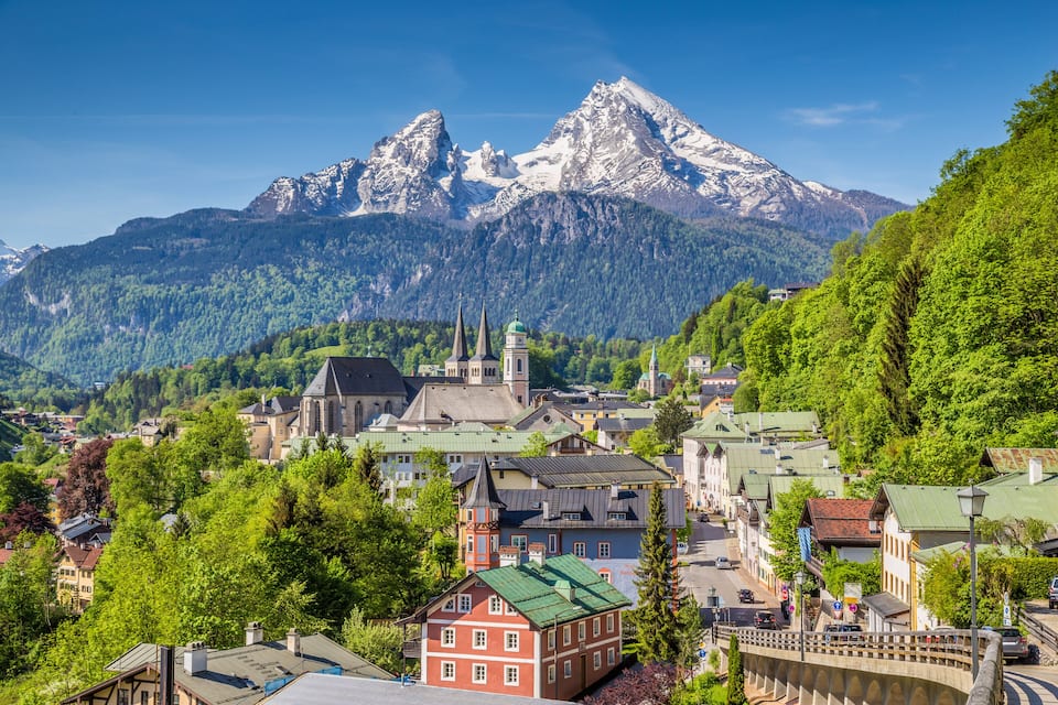 A town with a church, a bridge, and snow-capped mountains in the background.