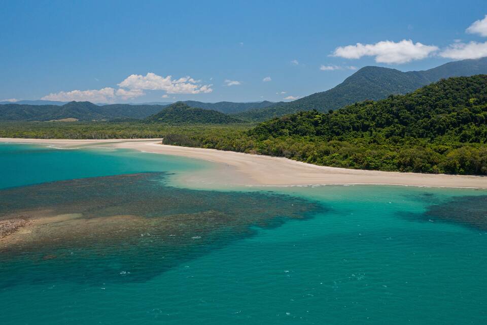A turquoise coastal area with a sandy beach and dense green forested hills in the background.