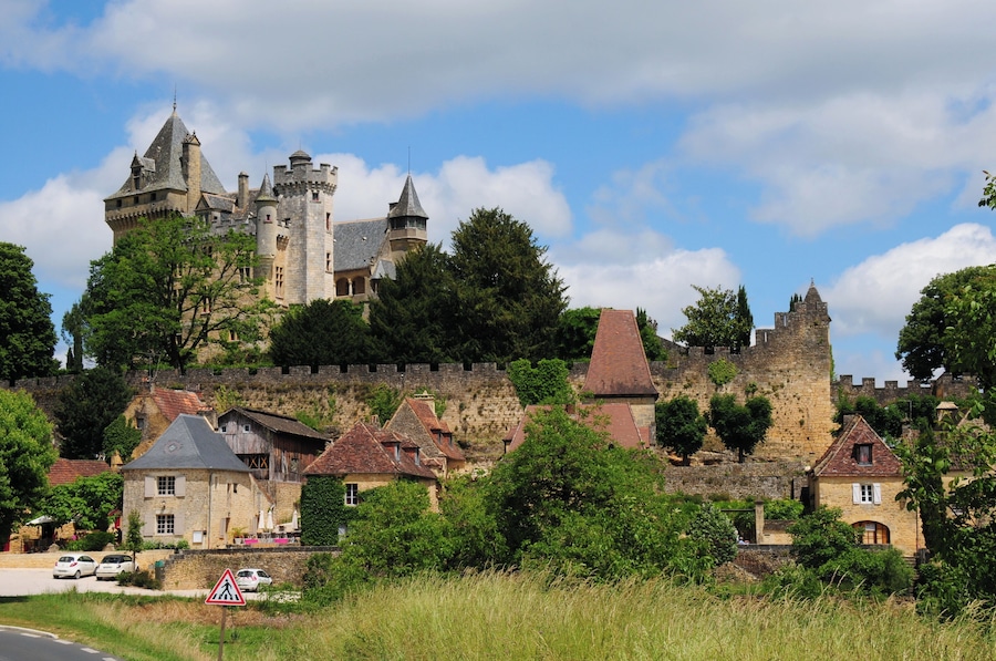 Un château historique, doté de tours et d’un mur d’enceinte, entouré de maisons traditionnelles en pierre.
