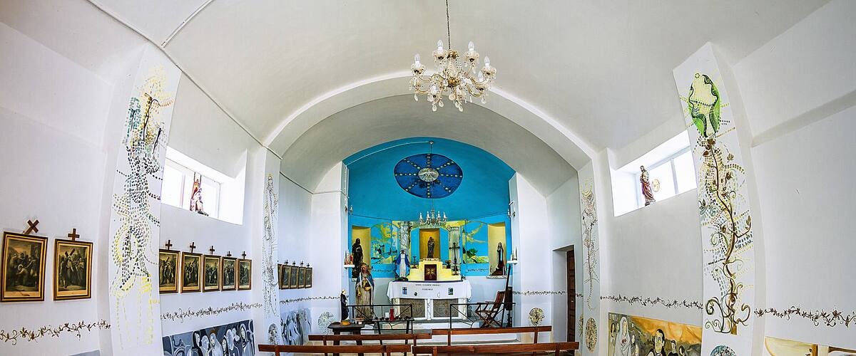 A church interior with wooden benches, a blue altar, and religious paintings.