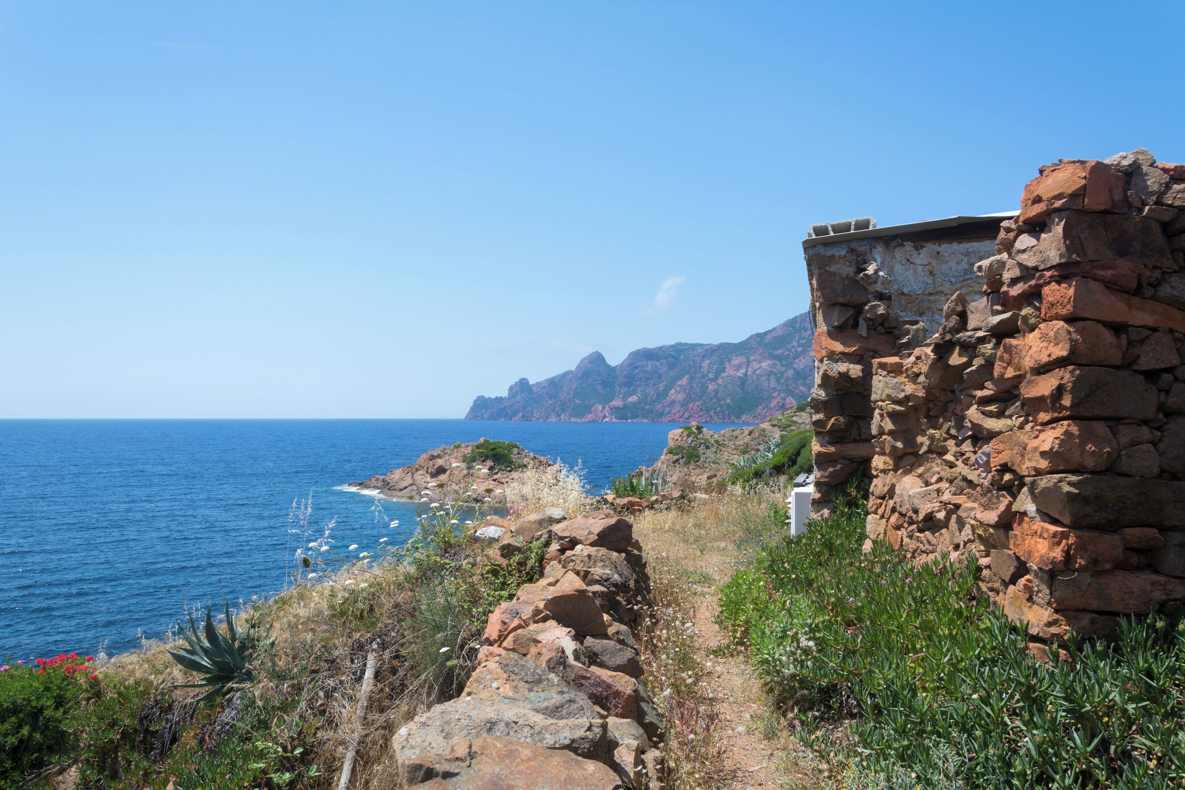 A coastal landscape with a stone wall, rocky terrain, and the ocean.