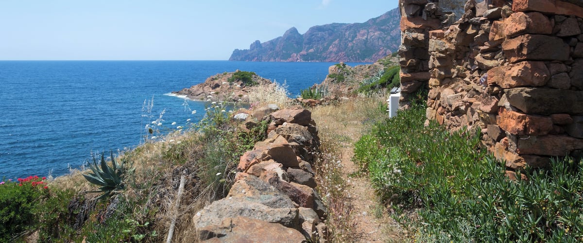A coastal landscape with a stone wall, rocky terrain, and the ocean.