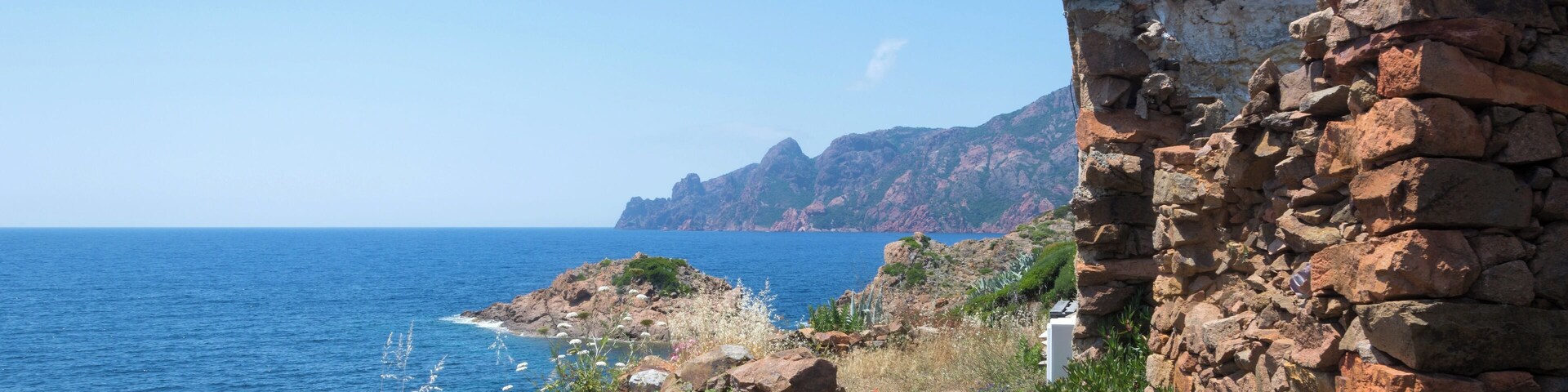 A coastal landscape with a stone wall, rocky terrain, and the ocean.