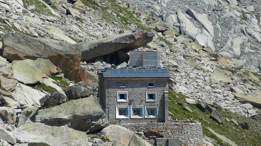 Een stenen gebouw met blauwe luiken, verscholen in rotsachtig terrein.