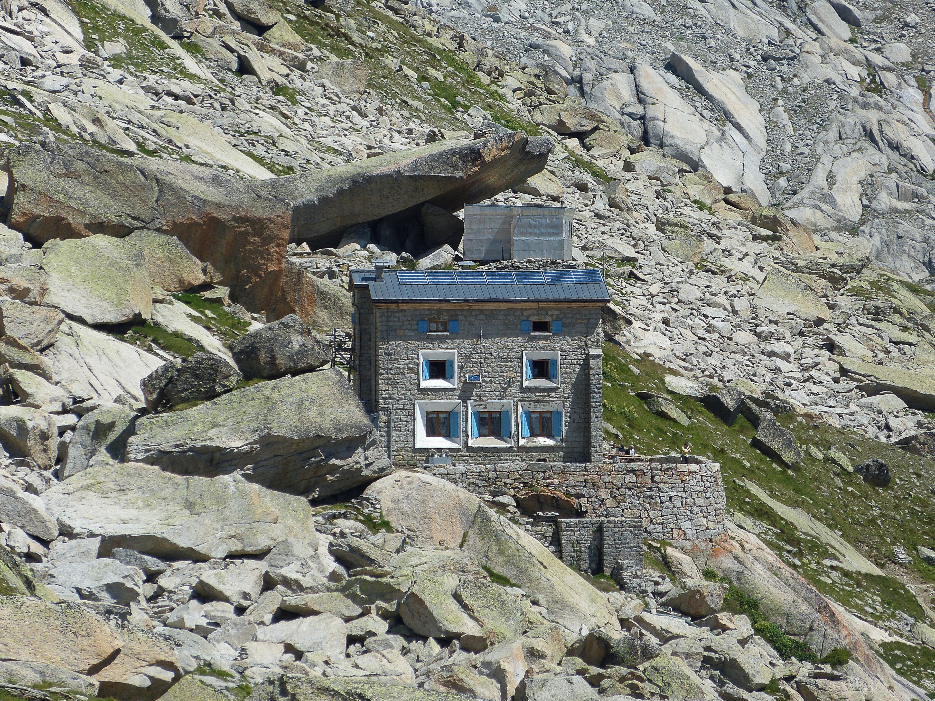 A stone building with blue shutters nestled among rocky terrain.
