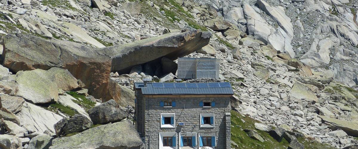 A stone building with blue shutters nestled among rocky terrain.