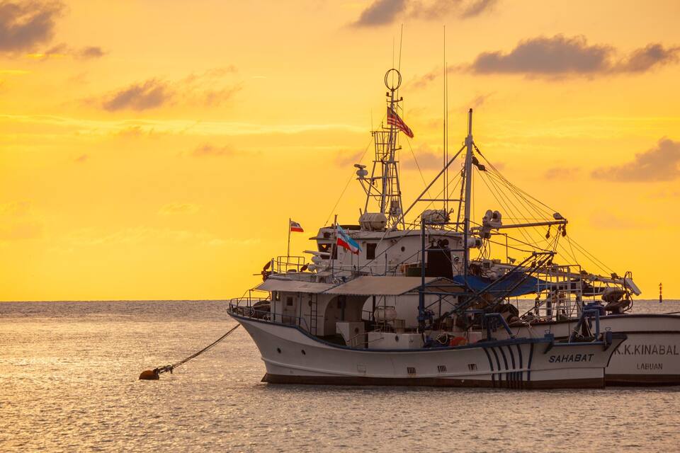 A fishing boat named K.K. Kinabalu sailing on the water during sunset.