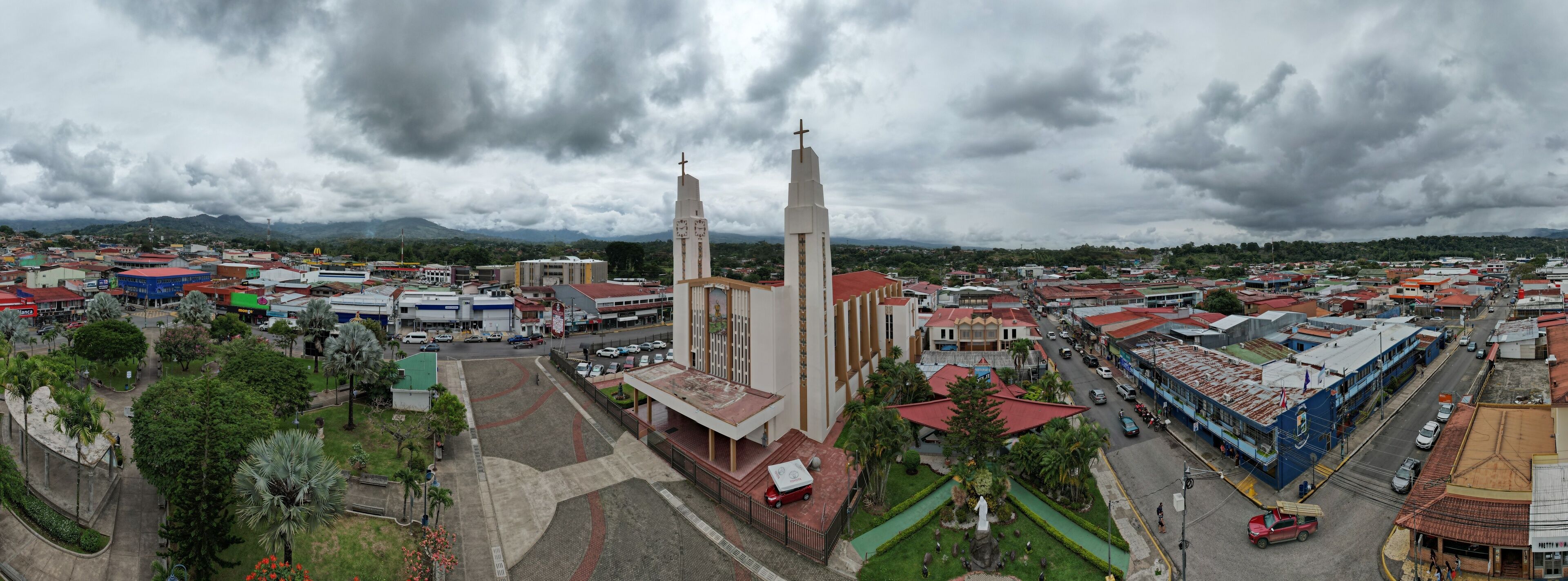A cityscape with a prominent church featuring two tall towers and a statue in front.