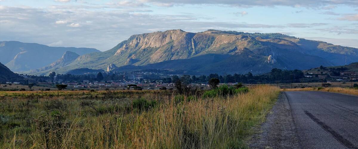 A rural landscape with a mountain range, a road, and scattered buildings.