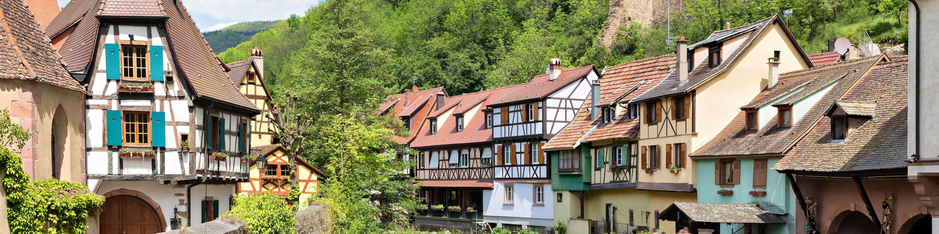 A picturesque European village with traditional half-timbered houses, a flowing river, and a castle on a hill.