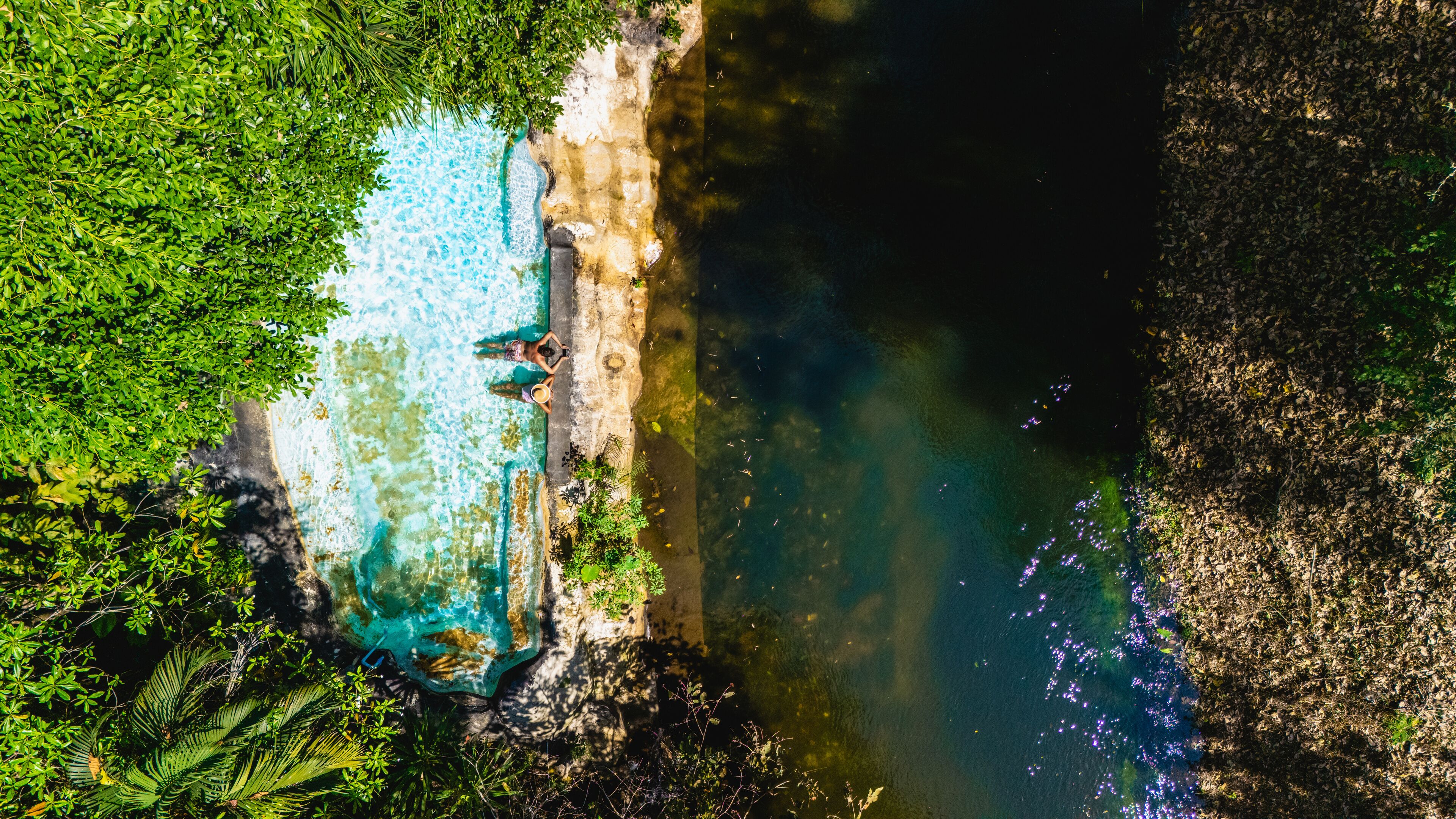 A river with clear turquoise water, surrounded by lush greenery and a rocky cliff.