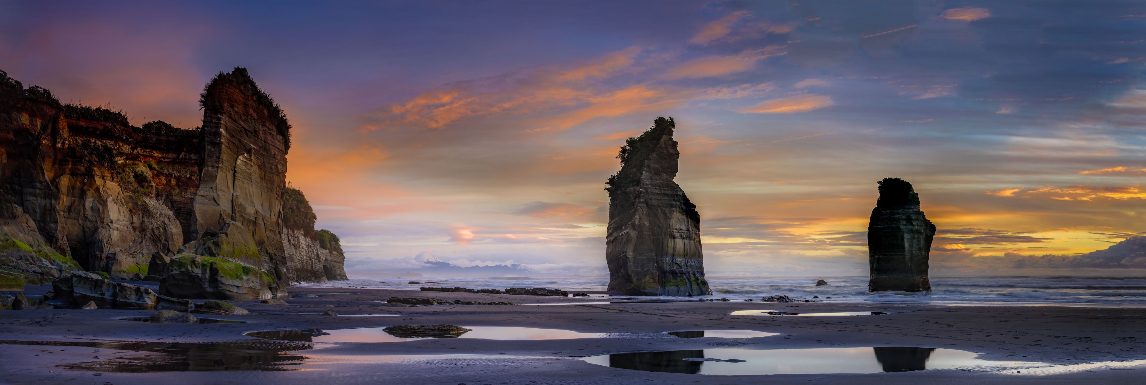 A coastal landscape with two prominent rock formations and a beach with reflective puddles.