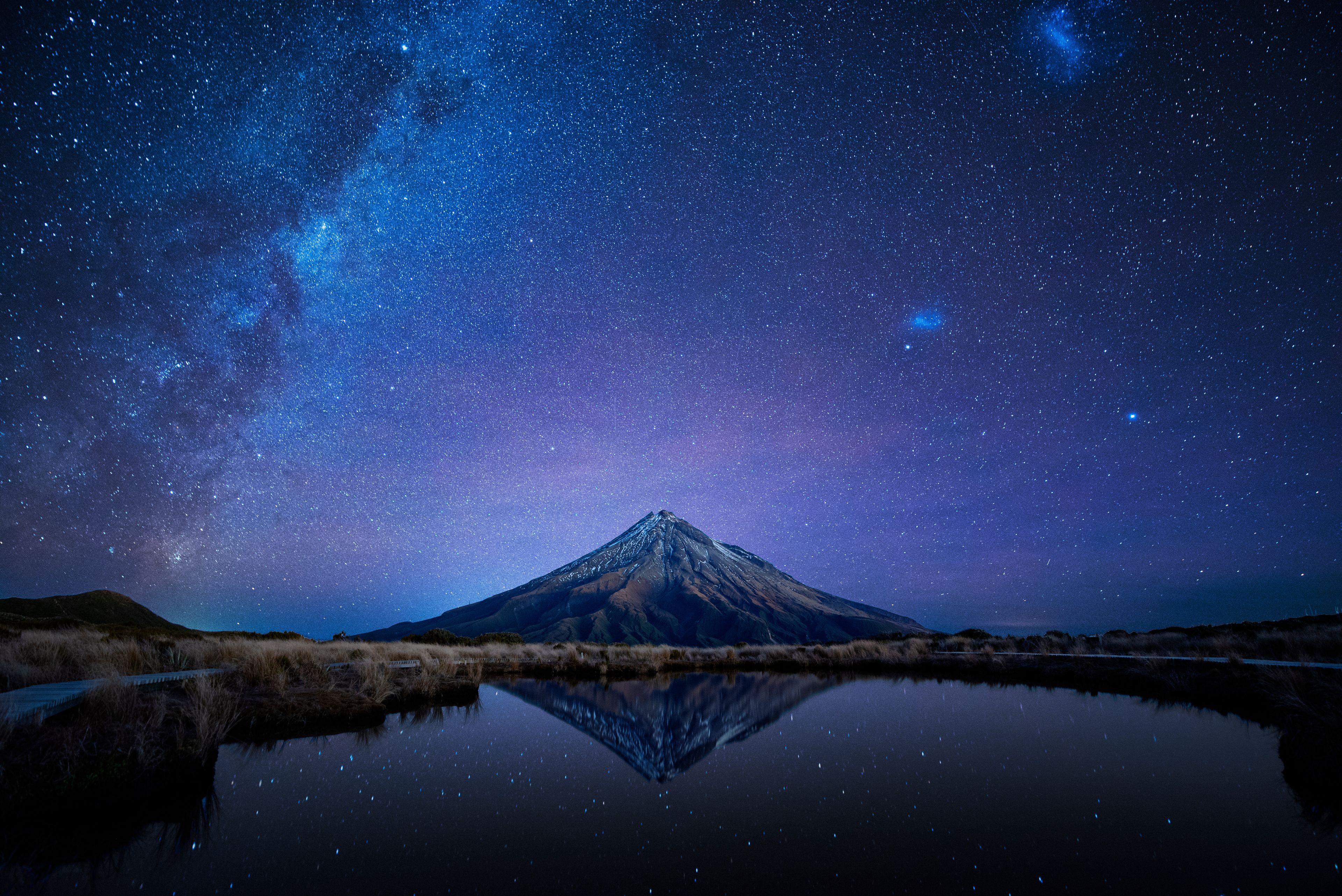 Cielo stellato sopra una montagna, con il suo riflesso in uno specchio d'acqua.