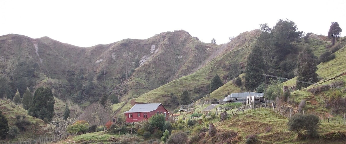 A red house on a hillside with a barn and fencing in the background.