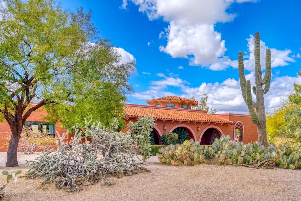 A desert landscape with a red-roofed building, cacti, and trees under a blue sky.