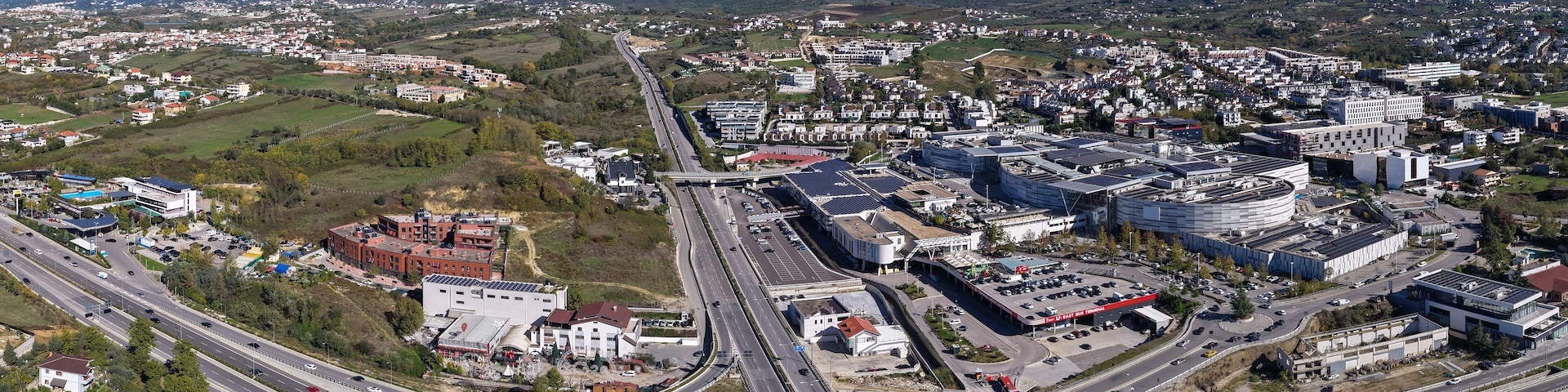 Paisagem urbana com um entroncamento rodoviário, edifícios e montanhas ao fundo.