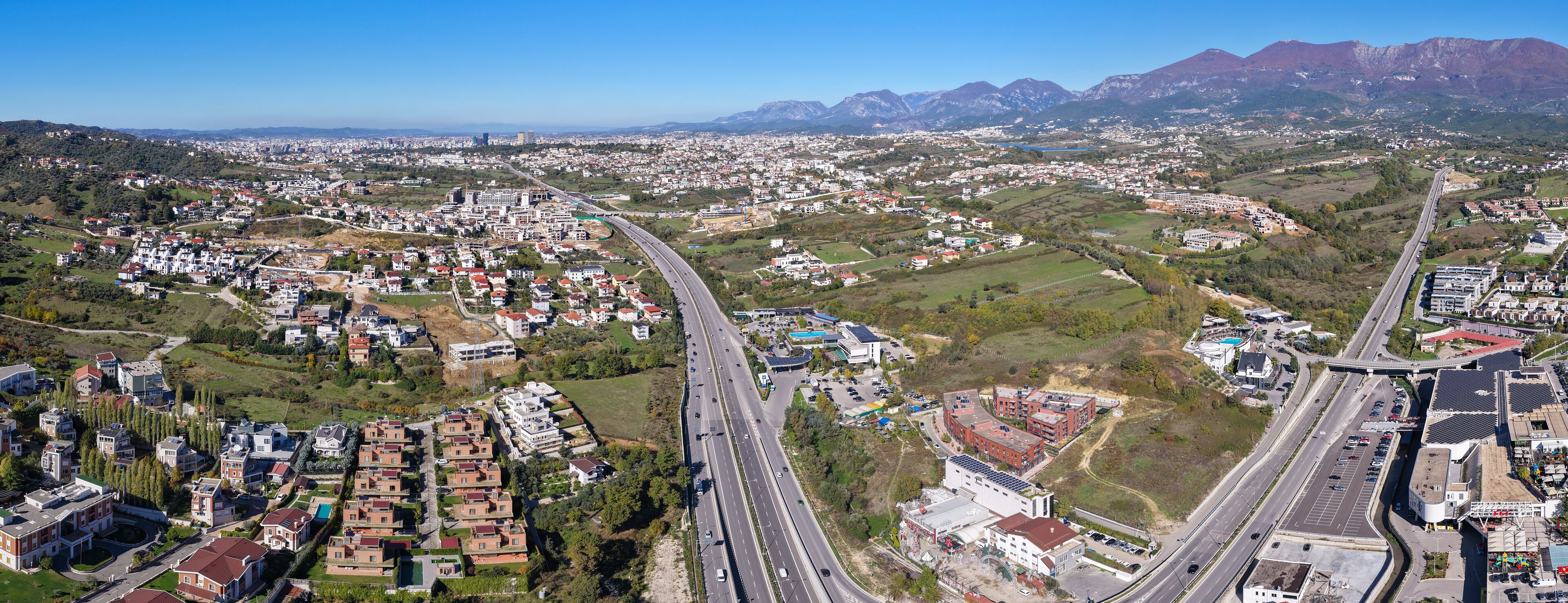 A cityscape with a highway, residential areas, and mountains in the background.