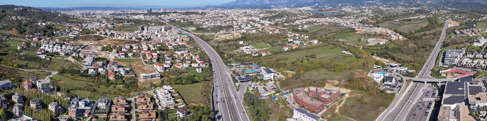 A cityscape with a highway, residential areas, and mountains in the background.