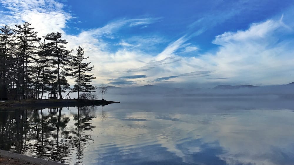 A calm lake with reflections of trees and a clear sky.