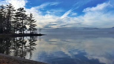 A calm lake with reflections of trees and a clear sky.
