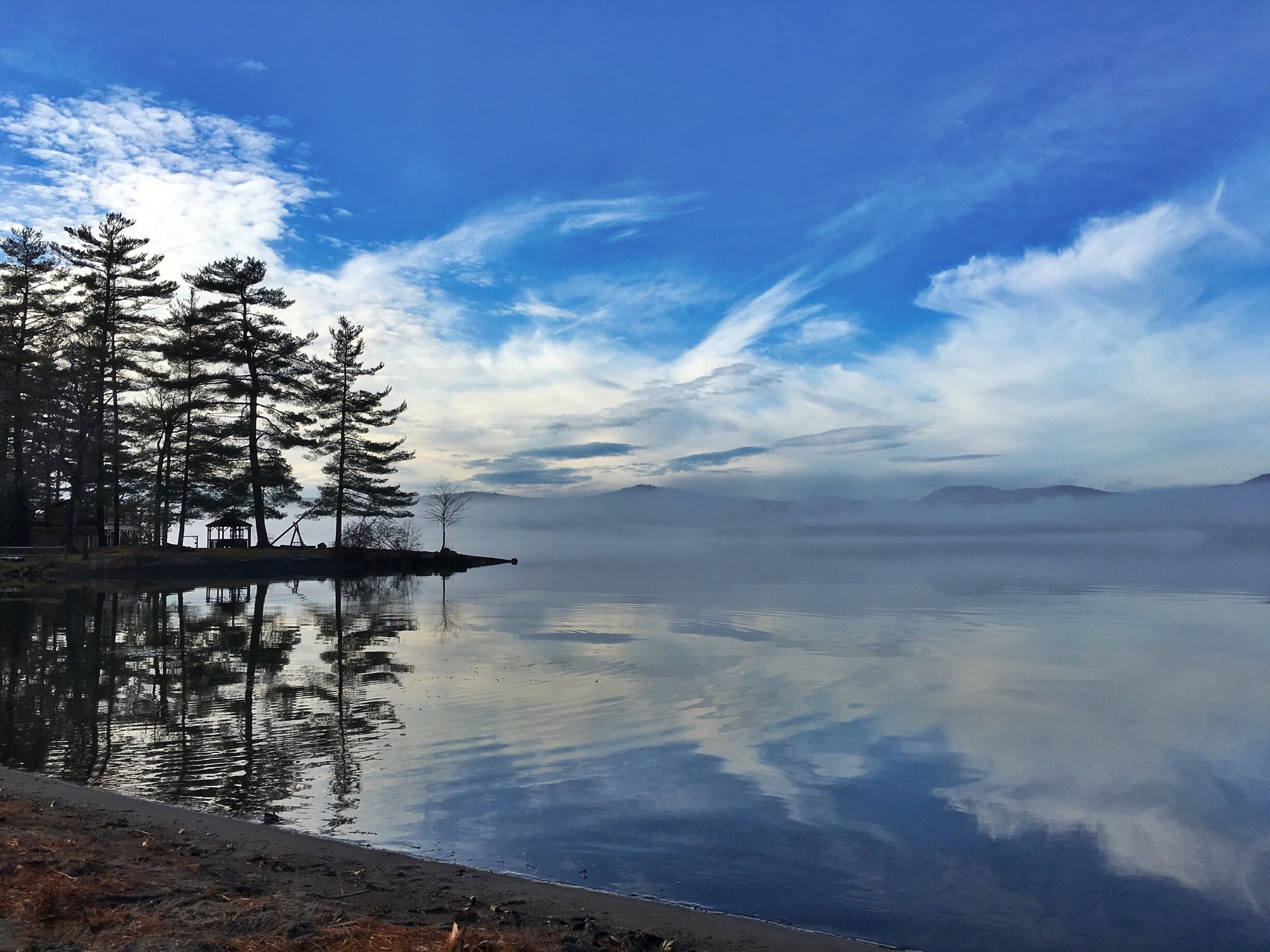 A calm lake with reflections of trees and a clear sky.