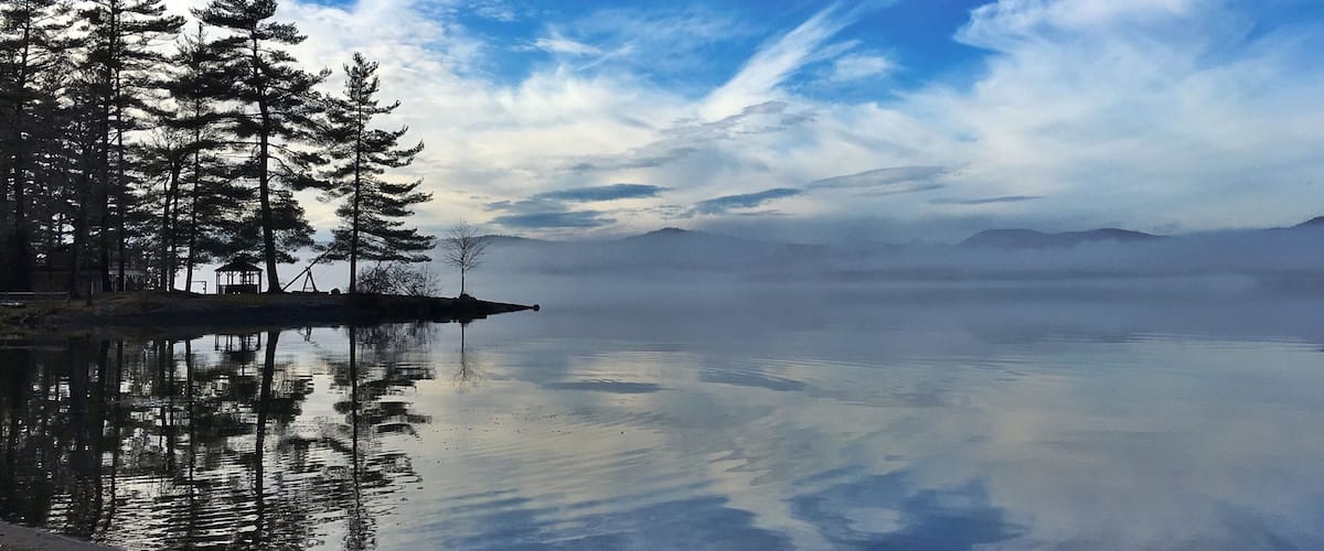 A calm lake with reflections of trees and a clear sky.