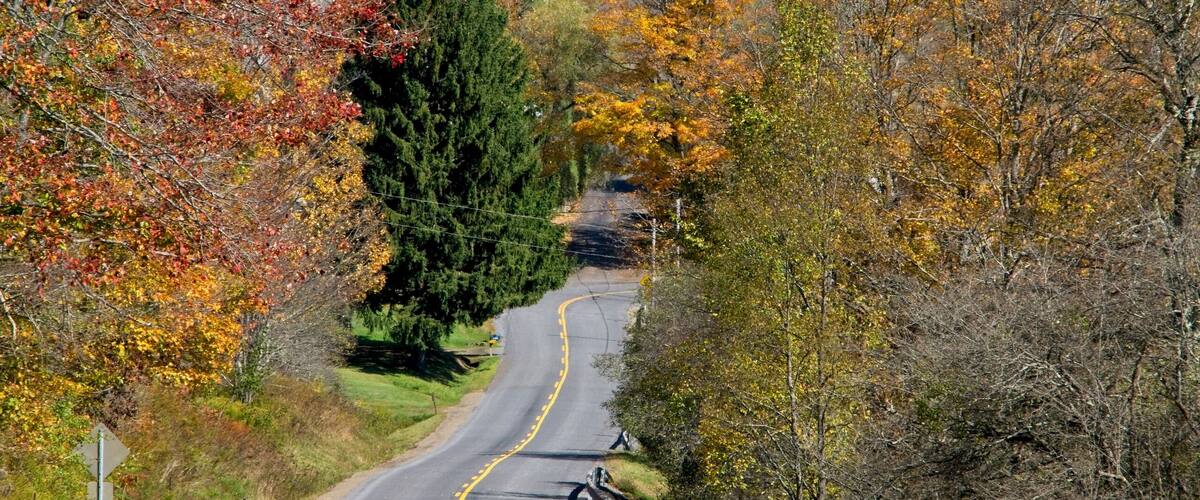 A winding road through a rural area with autumn foliage, a white house, and a red barn.