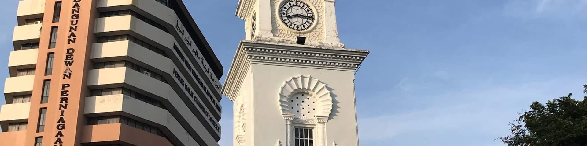 A historic clock tower with a dome and a sign reading "Bangunan Dewan Melayu Pulau Pinang."
