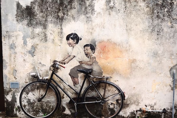 A mural of two children on a bicycle against a weathered wall.