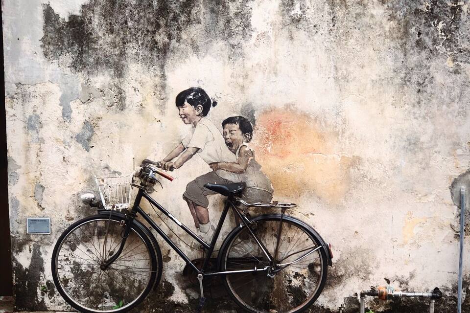 A mural of two children on a bicycle against a weathered wall.