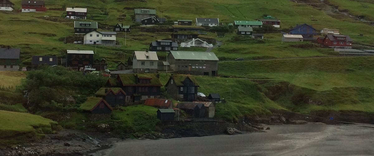A coastal village with houses on a hillside, a rocky shoreline, and a mountain in the background.