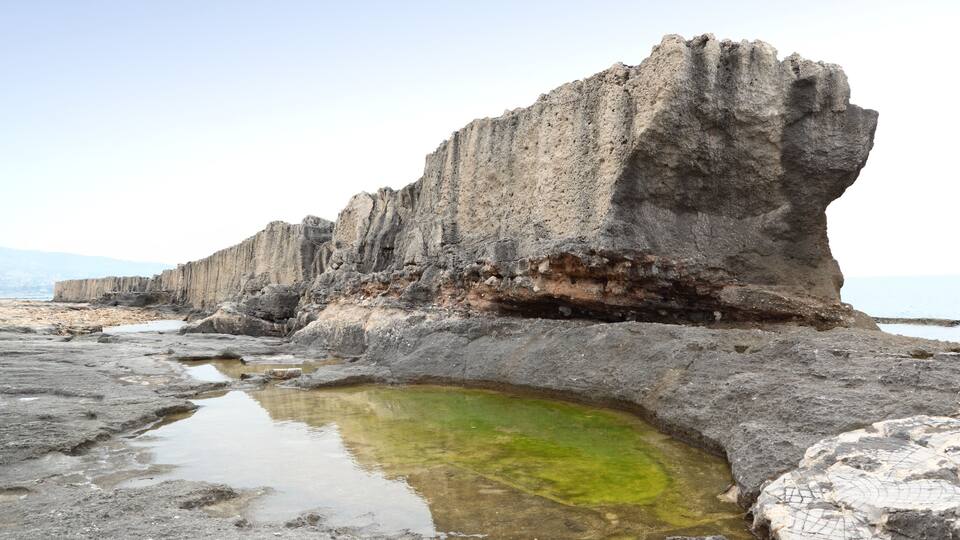 A rocky coastline with a large rock formation and a small pool of water.
