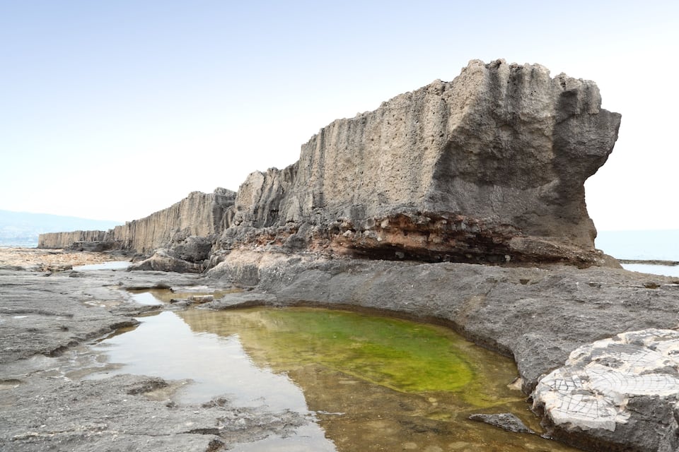 A rocky coastline with a large rock formation and a small pool of water.