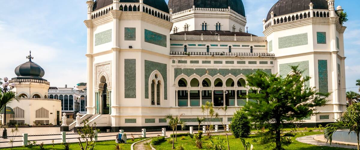 A large mosque with three domes and a white facade.
