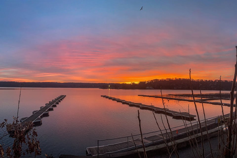 A sunset over a calm lake with wooden docks and a distant shoreline.