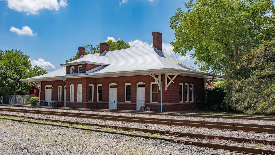 A red brick train station with white trim and a peaked roof.