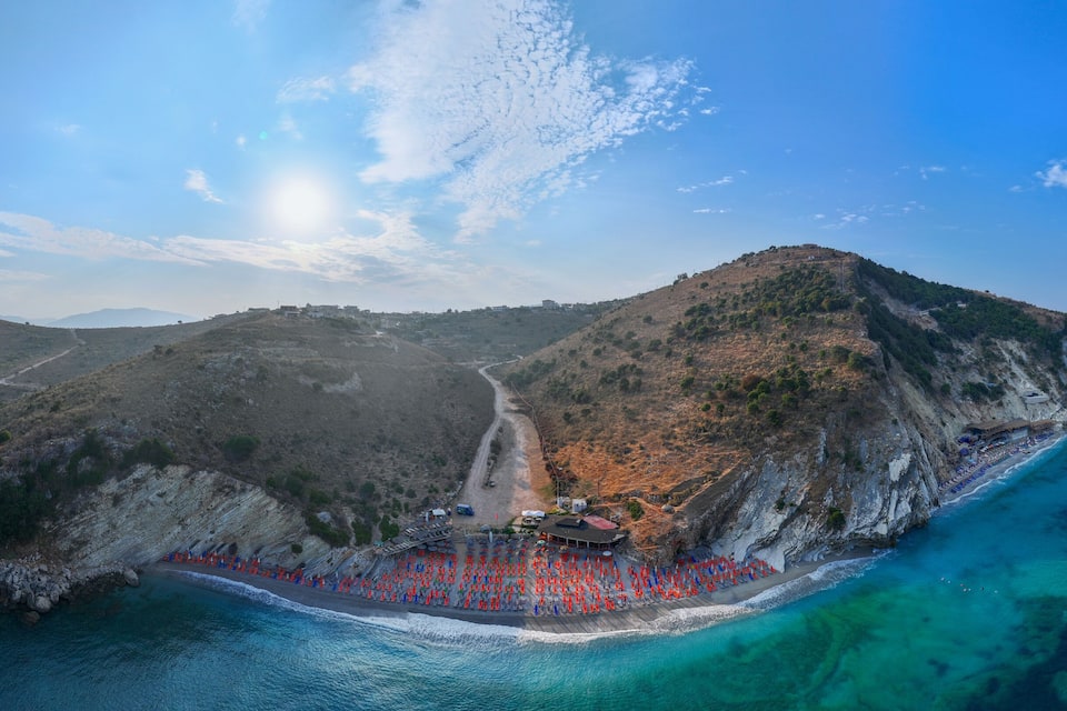 A coastal landscape with a beach, rocky cliffs, and a small settlement on a hill.