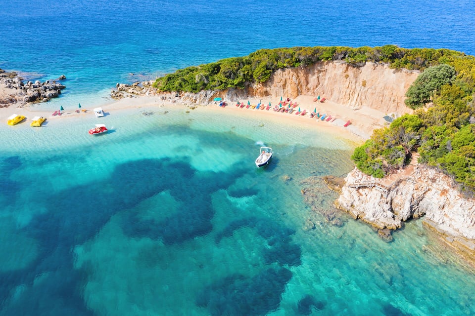 A coastal beach with clear turquoise waters, a boat, and colorful umbrellas.