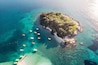 An island surrounded by clear turquoise waters with several boats anchored near the shore.